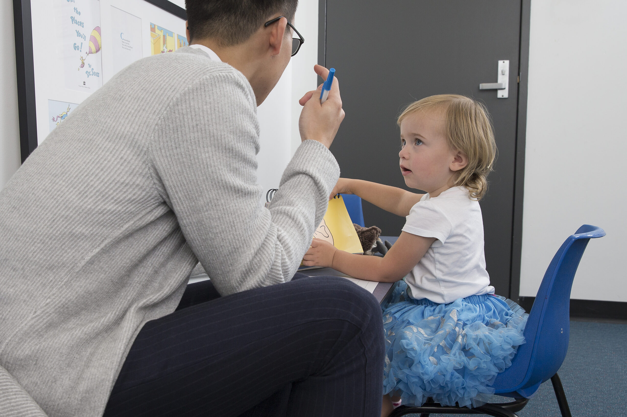 Male speech pathologist with girl toddler at table in speech pathology clinic
